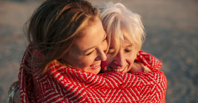 Dos mujeres de distintas generaciones compartiendo un abrazo envueltas en una manta durante al aire libre el atardecer, representando los beneficios de la desconexión digital y las rutinas de detox digital para recuperar el tiempo con seres queridos.