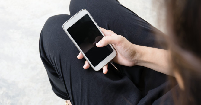 Persona sosteniendo un teléfono móvil con la pantalla oscura, ilustrando consejos y hábitos para ahorrar energía con los dispositivos que usamos a diario y reducir la factura de la luz.