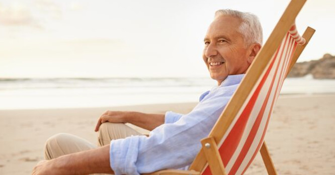 Hombre mayor sonriendo desde una tumbona en la arena de una playa tranquila al atardecer, representando la paz mental y la estabilidad financiera que se consigue al organizar los gastos con las mejores apps gratuitas para ahorrar.