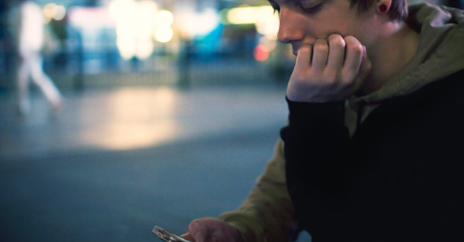 Hombre joven pensativo mirando la pantalla de su teléfono móvil de noche, representando cómo los usuarios interactúan con los algoritmos de las redes sociales.