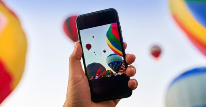 Mano de una persona sosteniendo un smartphone que muestra en su pantalla una fotografía nítida y colorida de globos aerostáticos, ilustrando la importancia de comparar la calidad de la cámara y la pantalla antes de comprar un móvil.