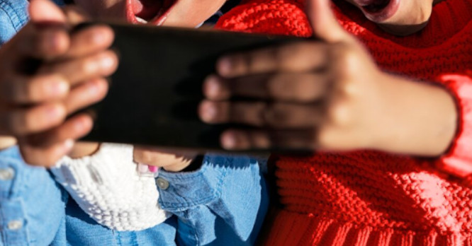 Primer plano desde un ángulo cenital de dos niños de la mano sosteniendo juntos un smartphone, ilustrando la importancia de educar sobre los riesgos de internet, qué es el sexting y cómo prevenirlo desde edades tempranas.