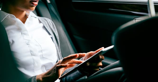 Primer plano de las manos de una mujer utilizando una tablet en la parte trasera de un coche, ilustrando la comodidad de gestionar la seguridad conectada y vigilar tu casa desde el móvil con cámaras de seguridad mientras viajas.